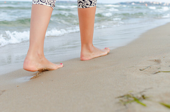 A person walking barefoot on the sandy beach along the sea shore.