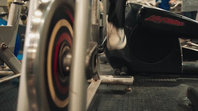 Low angle close up video shot of a spin bike flywheel spinning fast during an intense indoor cycling workout in a modern gym.