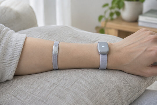 Adult forearm with fabric wristband and silver skin sensor on linen cushion, wearable biofeedback device, health monitoring concept