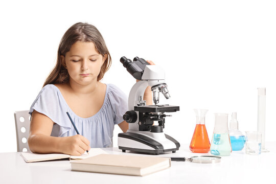 Young girl sitting at a desk with a microscope and lab flasks and writing in a notebook