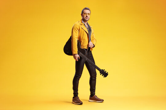 Man in a yellow jacket and leather pants holding an electric guitar