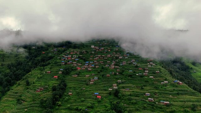 Drone shot of fog rolling over a green terraced village in Nepal.
