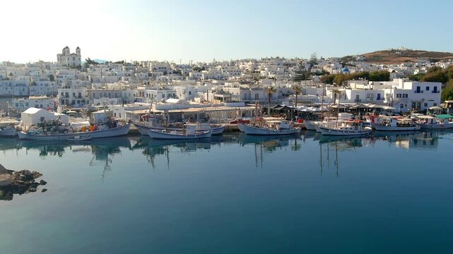 Aerial view of traditional fishing boats moored in the calm harbor of Naoussa with white buildings and blue sky in the background, Naoussa, Greece.