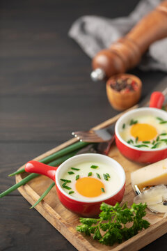 Oeuf cocotte. Baked eggs (Eggs in cocotte) with сheese and green onion in portion ceramic bowl on white background. Comfort food for breakfast