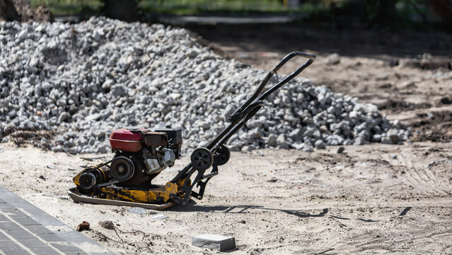 A machine stands in a dirt area next to piles of stones and gravel. Workers prepare for heavy construction tasks. Equipment is ready for use