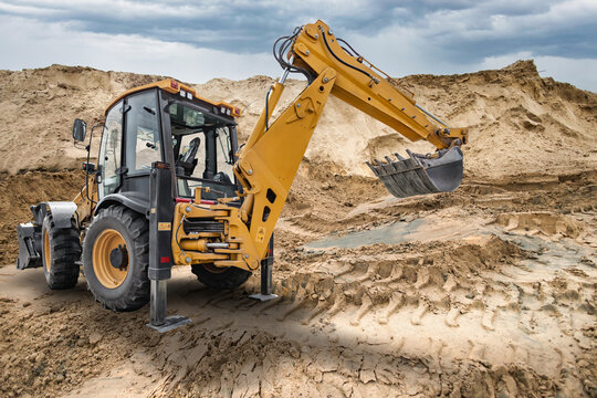 A universal excavator loader operates at a construction site. The machine moves dirt and debris while surrounded by a large pile of sand and earth