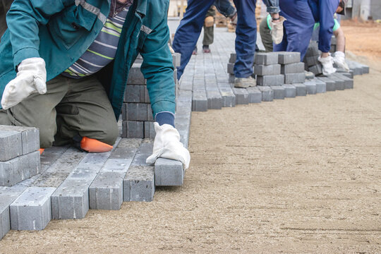 Workers laying gray bricks for a pavement project at a construction site during daylight hours