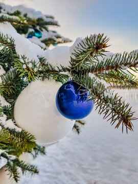 A natural Christmas tree stands decorated with ornaments and snow. It is winter, and the scene shows a festive atmosphere during the New Year celebration
