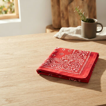 Red paisley bandana laid flat on a light brown wooden table in soft daylight