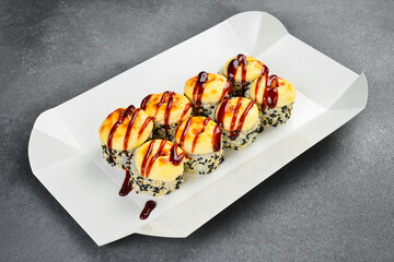 Baked sushi roll set with baked cheese topping and unagi sauce in takeaway box. Delicious Japanese rolls sprinkled with sesame seeds. Fresh gourmet Asian food. © Yaruniv-Studio
