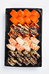 Large Japanese sushi roll set with salmon shrimp and unagi eel isolated on white background. Assorted rolls served in black takeaway tray. Fresh seafood. © Yaruniv-Studio