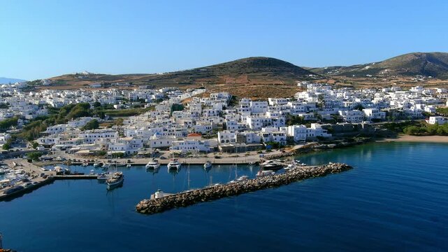 Aerial view of a traditional white village with a harbour and boats on the coast of Paros, Greece.