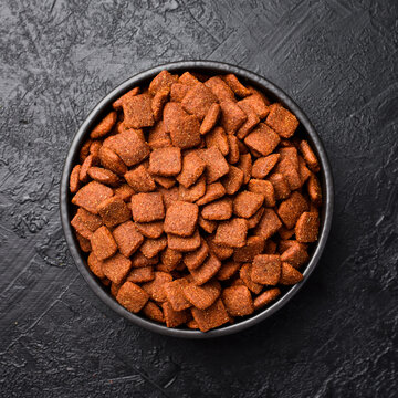 Dry dog ​​food. Bowl with dog food and various treats. On a black slate background. Top view.