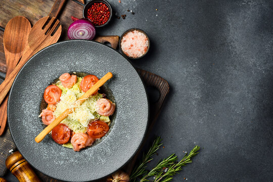 Caesar salad with salmon in a dark stone plate. Top view. Free space for text.