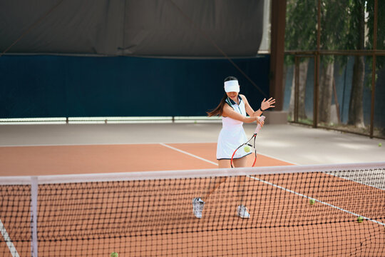 Asian Woman Playing Tennis on Clay Court, Hitting Ball with Racket Near Net