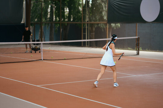 Asian Woman Playing Tennis on Clay Court During Training Session with Coach