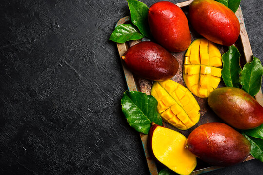 Mango tropical fruit with leaves on black textured stone background. Top view. Free space for text.