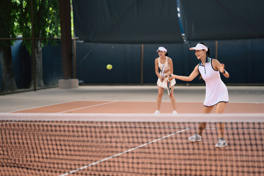 Asian Women Playing Tennis Doubles Match on Indoor Court During Daytime