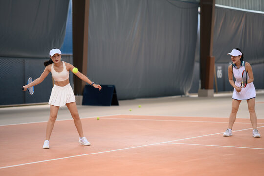Two Asian Women Playing Tennis Doubles on Indoor Court, Active Sporty Lifestyle