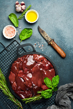 Raw fresh turkey liver in a frying pan, ready to cook. Top view. On a dark textured stone background.