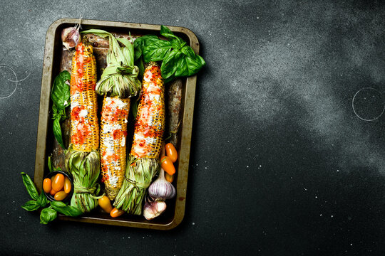 Barbecue. Grilled corn with spices and sauces on a black stone background. Organic food. Top view.