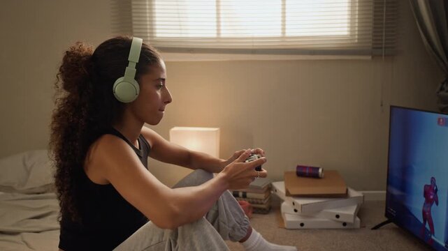 Young multiethnic woman wearing headphones playing video game with gamepad controller on TV. Footage suitable for gaming gear promotions and leisure lifestyle campaigns