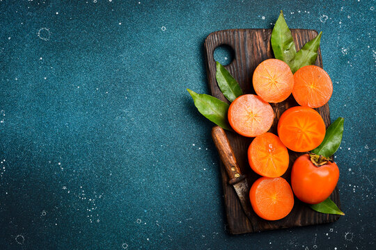 Close-up, Sliced ​​persimmon fruits on a wooden cutting board. Close-up. Rustic style, on a dark background.