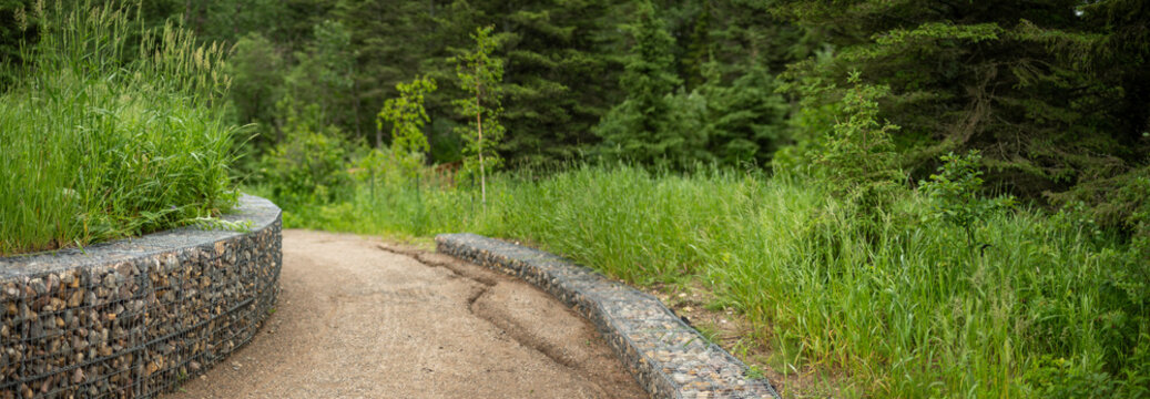 Looking down a curving walking trail bordered by gabion rock walls set in a park forest
