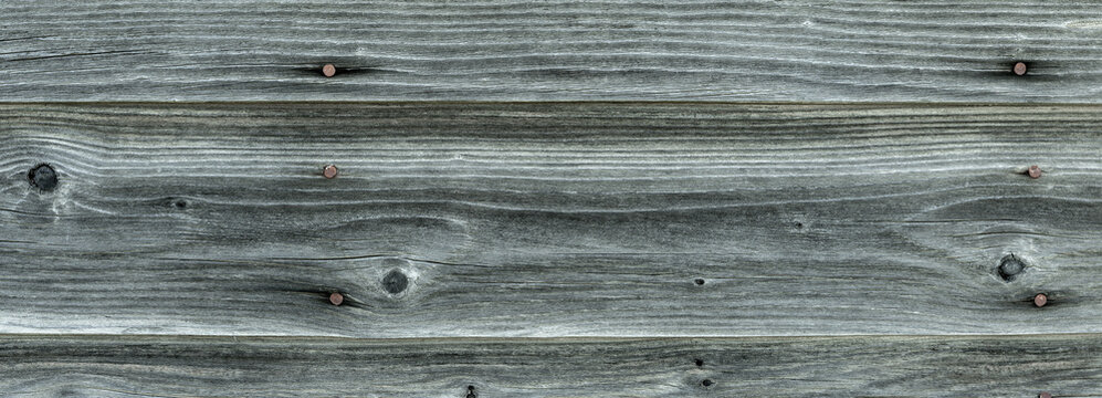 Close-up of gray wooden wall with weathered planks and rusty nails creating a background pattern
