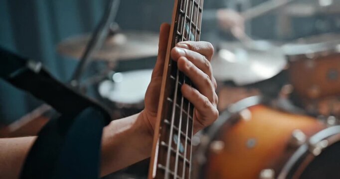 Close-Up of Musician's Hand Playing Bass Guitar on Stage with Blurred Drum Kit Background