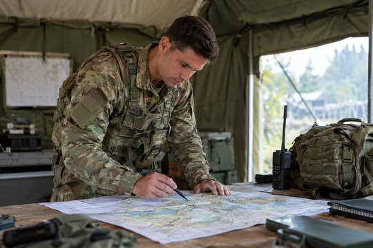 Soldier in camouflage uniform studying tactical map in military tent