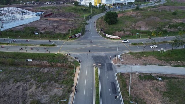 Aerial top view of a four-way road intersection with vehicles and motorcycles crossing a yellow box junction in a developing suburban area with