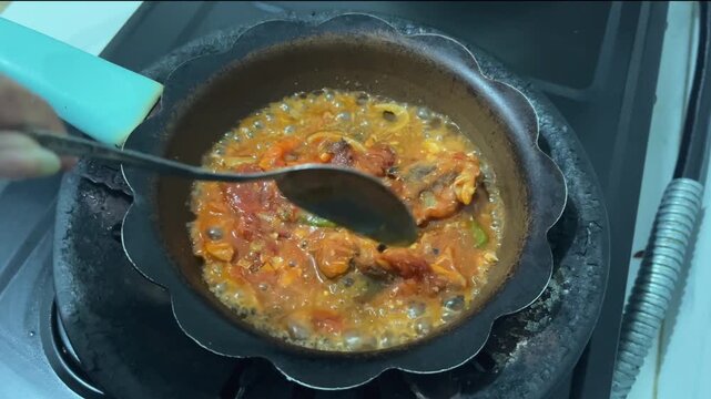 Close-up video of sardines simmering in a flavorful tomato sauce while being gently stirred in a pan on a kitchen stove. Homemade cooking and seafood preparation concept.