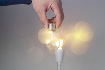 Hand holds glowing light bulb against soft bokeh background. © jittawit21