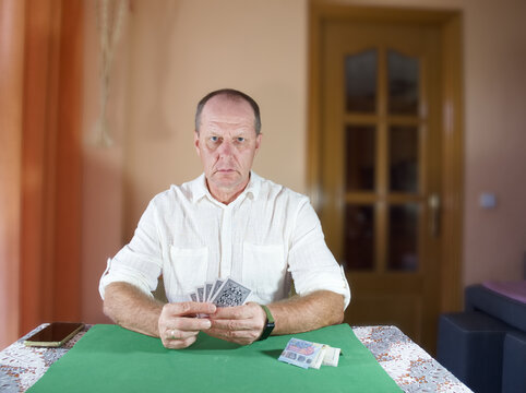 Man plays cards at a table in a room with warm colors and simple decor during the afternoon