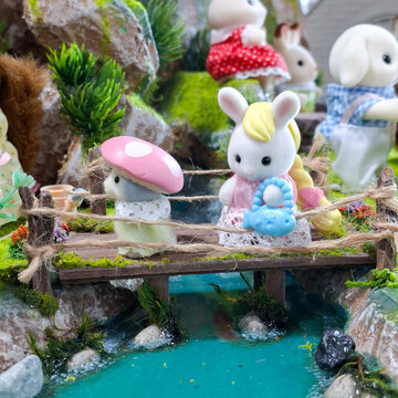 Sylvanian Families cute bunny toy figures standing on miniature wooden bridge crossing clear blue stream in fairytale mossy forest landscape diorama on September 27, 2026 in Bangkok, Thailand.