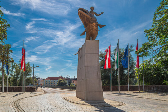 Simbach am Inn, Germany &ndash; August 26, 2025: The sculpture "Aenus reitet auf einem Huchen" (Aenus riding a huchen), located before the bridge over the Inn River that leads to Braunau am Inn, Austria.