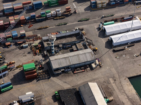Aerial view of the industrial port area with stacked shipping containers, warehouses, a control tower, and cargo storage in Bajos de Haina, San Cristobal Provinc, Dominican Republic.