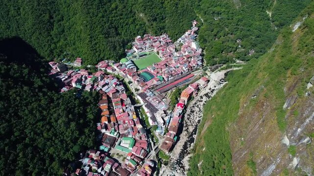 Aerial view of Aguas Calientes nestled in the Andes mountains with a river flowing through the town and lush green mountain slopes in Aguas Calientes, Cusco, Peru.