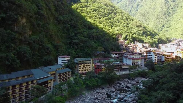 Aerial view of the town of Aguas Calientes nestled in a lush valley with a rocky river and dense mountain forests in Aguas Calientes, Cusco, Peru.