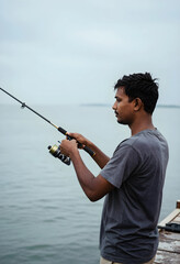 Fototapeta premium Leisure and patience, man fishing with a rod on a wooden pier by the sea for relaxation and outdoor recreation in a calm coastal environment
