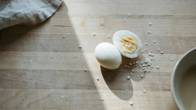 Hard-boiled egg half with salt and white ceramic bowl on wooden surface