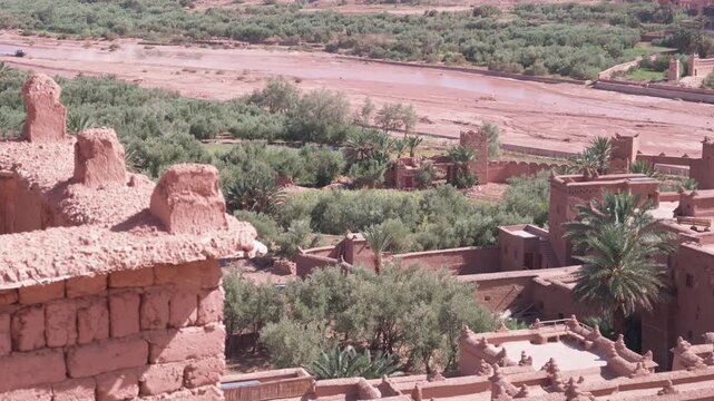 High angle panoramic view of the ancient ksar of ait benhaddou with a jeep driving along the riverbed and the traditional moroccan mud brick architecture in the desert