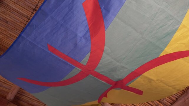 Amazigh berber flag with blue, green, and yellow stripes and a red tifinagh letter yaz, representing the imazighen culture and identity of north africa, waving