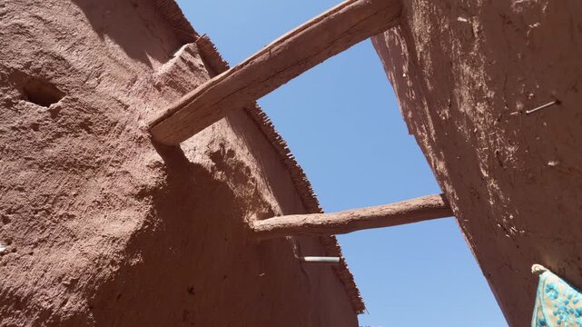Traditional mudbrick architecture of a berber kasbah in morocco with wooden beams supporting the walls against a clear blue sky, showing local handicrafts for sale