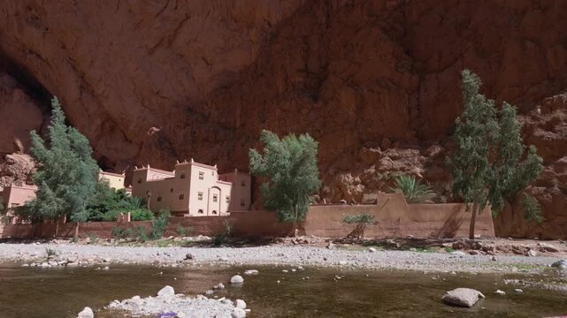 Traditional moroccan riad built into the rock walls of todra gorge, featuring distinctive berber architecture, nestled by a serene river in the atlas mountains