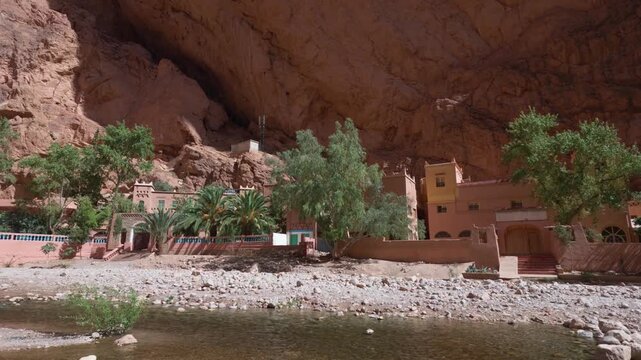 Todra gorge with traditional moroccan riad architecture nestled at the base of the red rock canyon walls alongside the dades river on a sunny day in the high atlas mountains