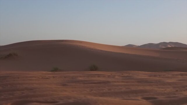 Strong wind blowing sand across desolate desert dunes under a clear sky during a mesmerizing sunset, evoking a sense of powerful, raw, and untouched nature