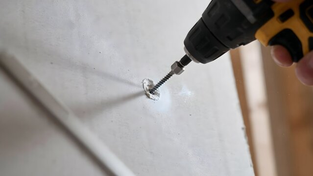Person using cordless drill to drill into drywall wall indoors during home renovation