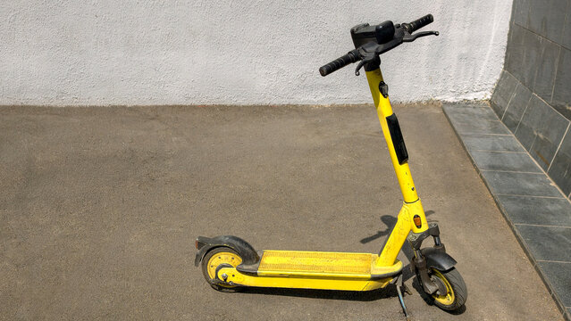 Yellow electric scooter parked on asphalt street, offering urban micromobility, sustainable transportation, and convenient last mile commute solutions for city dwellers